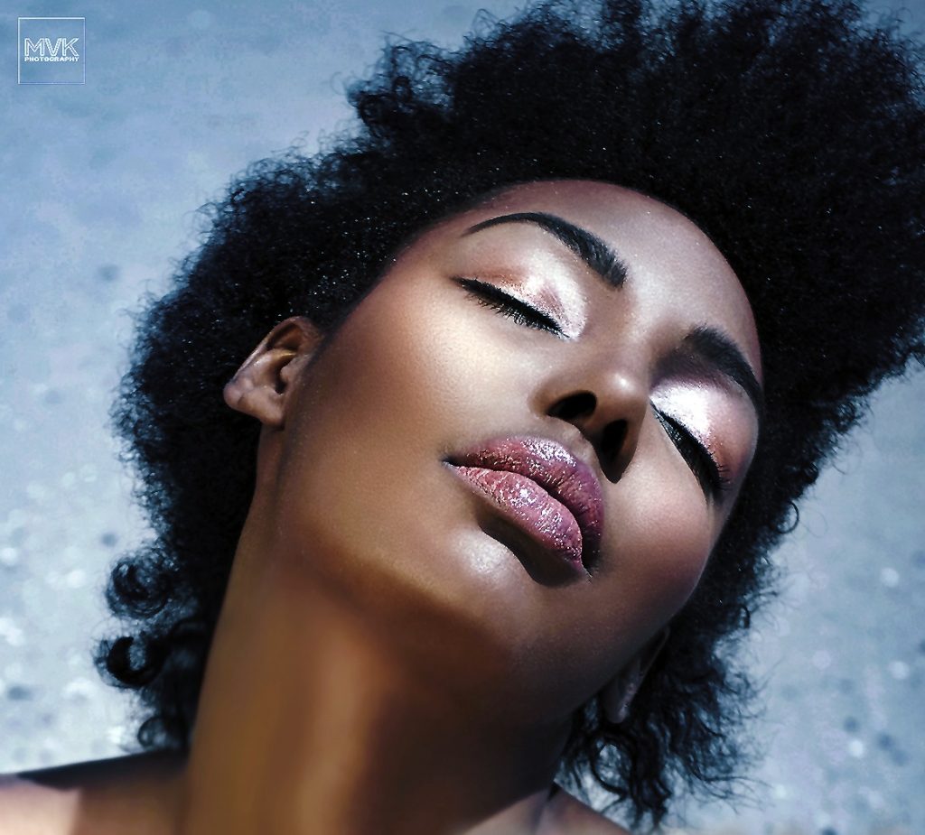 Black model on beach with shimmery eyeshadow and lipgloss